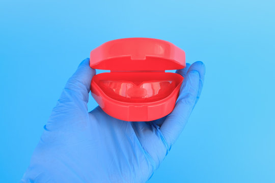 Doctor's hand in a blue glove holds a myofunctional trainer for teeth correction. Blue background. Selective focus.