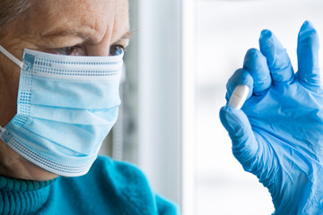 Fototapeta premium senior woman with mask and medical gloves holding pill in hand
