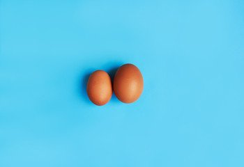 Brown eggs on blue background. Size difference concept between two farm eggs.