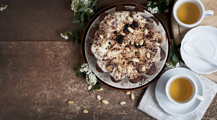 Chocolate cake with peanuts on table with tea and flowers on dark brown background. Top view