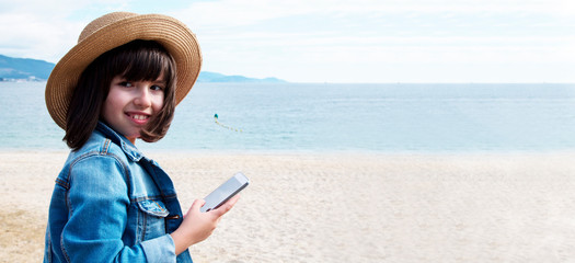 girl in hat and denim jacket using mobile phone on the beach