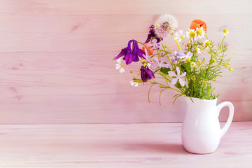Still life, a bouquet of wild flowers in a white jug. Bouquet of daisies, dandelions and bluebells