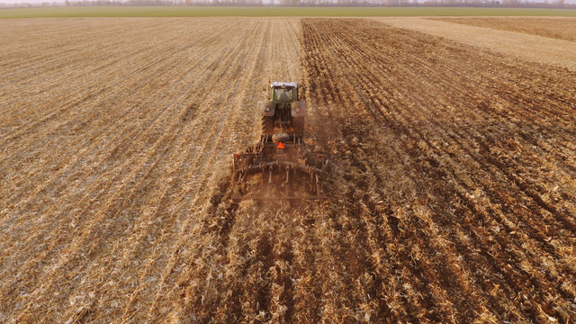 Tractor plowing field after harvesting. Back view of farming tractor working in field. Top view.