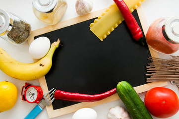 Slate, tomatoes, banana, red paper, lemon, egg, fork, clock, pasta, garlic, spices and cucumber on white background. Cooking at home. Cook. Vegetables and fruits. Flat lay food. Recipe. Ingredients 