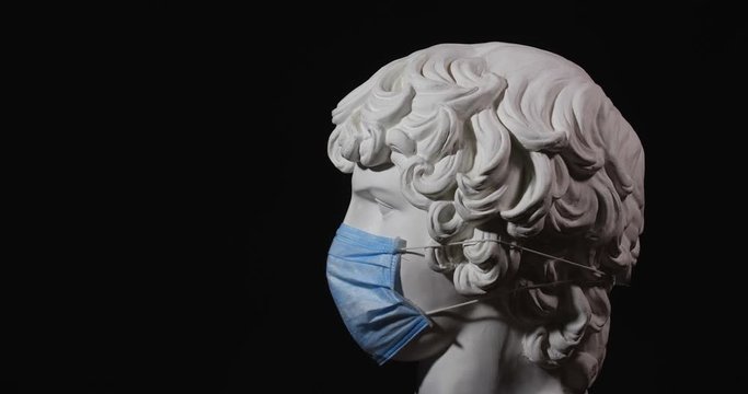 Epic studio close up shot of rotating gypsum head with dramatic light wearing medical face mask. Rotation of white antinous sculpt with face shield on it. On black background isolated 4k