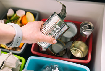 The woman throws the tin can to the one of four container for sorting garbage