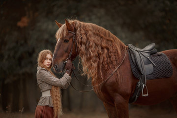 Beautiful long-haired blonde young woman in English style with red draft horse in autumn forest - 349482377