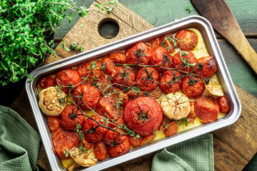 Tomatoes roasted on baking tray with garlic head and thyme. Rustic background
