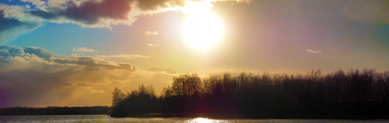 Fototapeta na wymiar Panorama: Cloudy sky, scenic sunset, forest and lake.