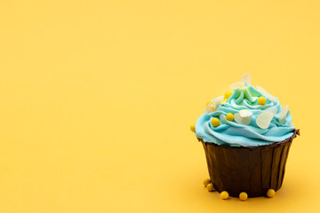 Blue cupcake decorated with candies on bright yellow background. Horizontal with space for text