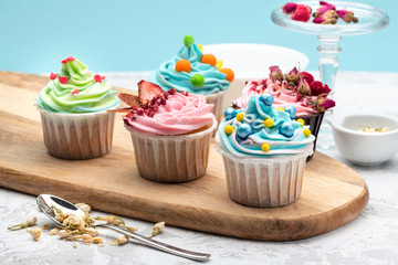 Colorful cupcakes with different modern decoration on wooden board with spoon and ingredients on blue background