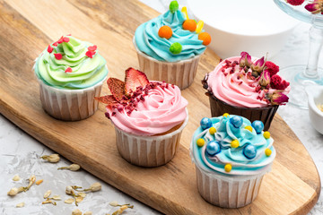 Colorful cupcakes with different modern decoration on wooden board with ingredients on blue background