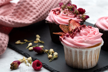 Pink cupcakes decorated by sublemented berries  and buttons of dry flowers on stone board with textile napkin