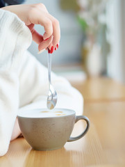 a girl in a white blouse is stirring sugar in a coffee Cup with a spoon. the wooden table. close-up.