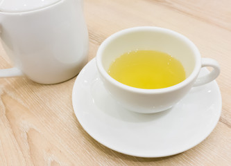 Cup of Japanese green tea and teapot on brown wooden table.