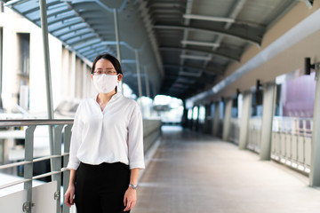 young beautiful asian woman with smiling face and wearing face mask as a social distancing guideline. She is walking on sky walk to train station. new normal, covid-19, coronavirus concept