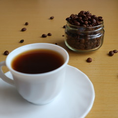 A white cup of black coffee and roasted coffee beans in the small jar