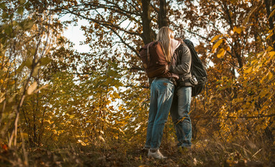 Kiss of backpackers in love hugging while standing alone against the backdrop of autumn forest outdoors