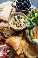 Closeup view of a wooden snack table full of delicious spanish food focused on a hummus bowl with poppy seeds on the top.
