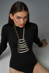 A ravishing brunette lady in a black bodysuit and a trendy choker is sitting on the gray floor. The...