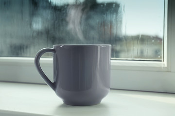 Obraz premium Cup of hot drink near window on rainy day