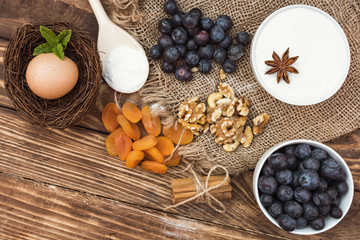 Egg in a nest, blueberries, flour in a bowl, dried apricot, nuts, cinnamon sticks and anise on wooden background