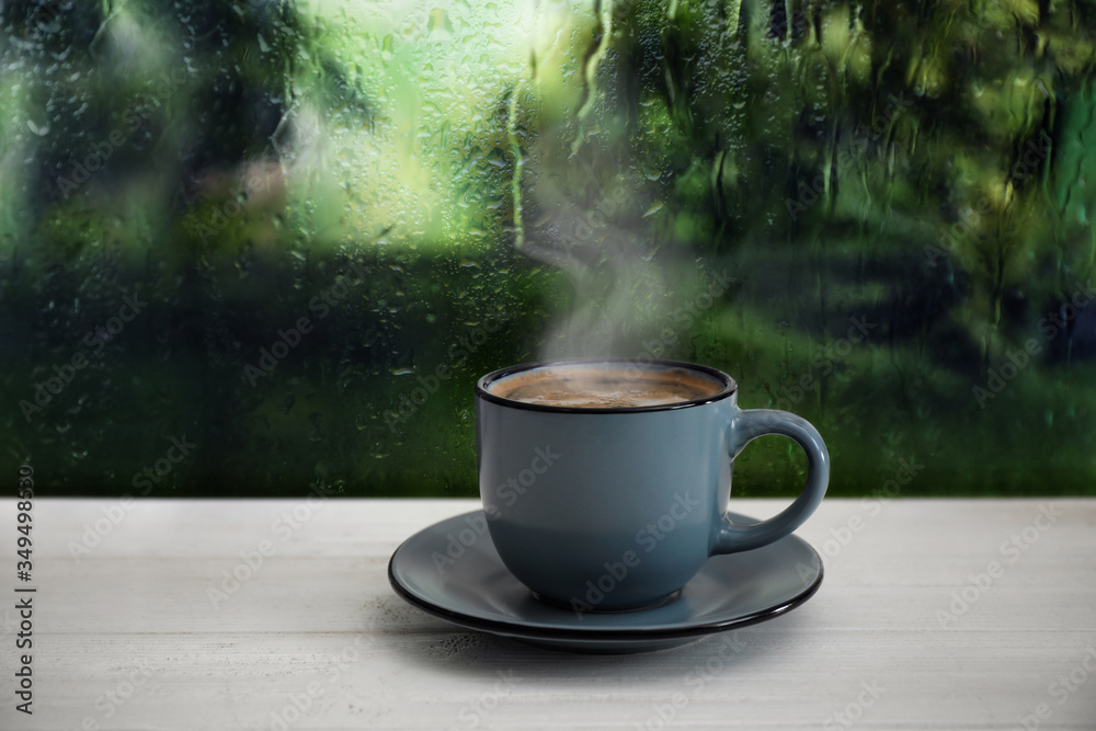 Wall mural Cup of hot drink near window on rainy day