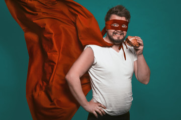 Hungry super hero man eating a hamburger, super hero or antihero in a red suit with a flying cloak...