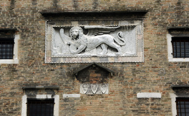 Historical brick facade with relief of winged lion and windows in Venice.