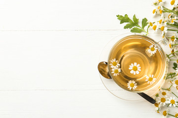 Flat lay composition with cup of tea and chamomile flowers on white wooden table. Space for text