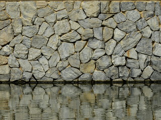 old stone wall with water reflection in the pond