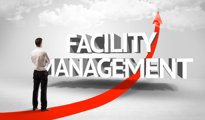Rear view of a businessman standing in front of FACILITY MANAGEMENT inscription, successful business concept