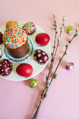 Close up of still life with Pysanka, decorated Easter eggs, dry willow branches and chocolate egg on pink background. Top view of egg wax resist technique, traditional for Eastern European cultures.