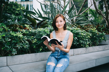 Smiling Asian woman holding book and looking at camera