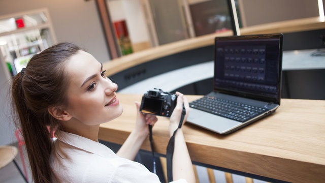 Cute young girl working at a laptop and holding a camera in her hands. Blogger and photographer,