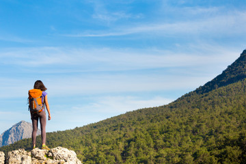 Naklejka premium A woman with a backpack stands on top of a mountain and admires the beauty of a mountain valley.