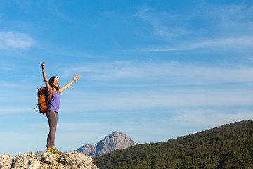 A woman with a backpack stands on top of a mountain and admires the beauty of a mountain valley.