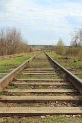 Obraz premium The railway stretching into the distance against the background of young green grass and trees in spring.