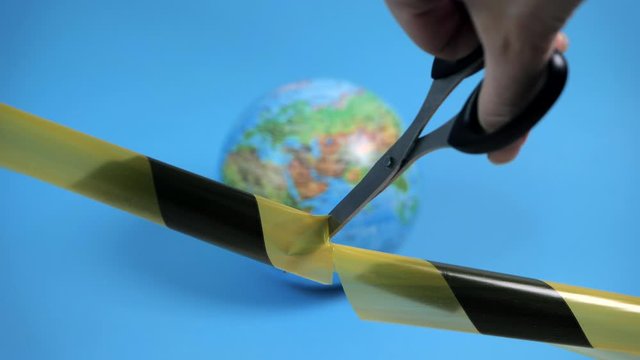 Quarantine cancellation. A hand with scissors cuts a black-yellow ribbon. Planet earth on a blue background.