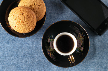 Coffee, oatmeal cookies and a smartphone on a blue background, top view