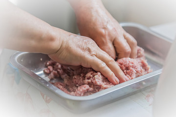 Hands knead minced on white background for concept design. Female put meat in a meat grinder