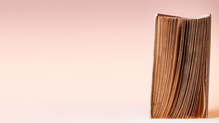 Naklejka premium Banner with opened old book. Book with shabby covers and ragged pages on light pink background with copy space.