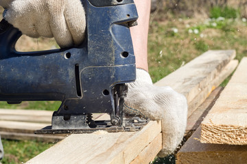 A male carpenter works with an electric jigsaw, sawing a tree.