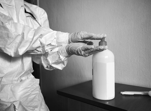Black and white cropped image of doctor in PPE suit, gloves, decontaminating hands with alcohol sanitizer. Preventive measures against coronavirus. COVID-19 concept