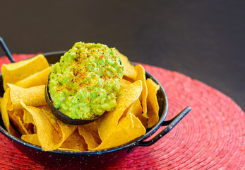 Nachos with avocado in black metal bowl, guacamole