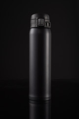 Black thermos on a black background with reflection. Thermo mug for coffee or tea.
