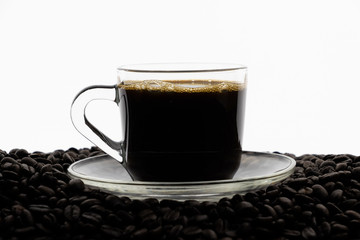 Black coffee with foam in clear glass cup on coffee beans field with white background