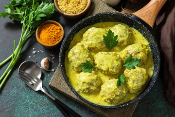 Meatballs with bulgur in sour cream and turmeric sauce in a pan on a dark stone countertop.