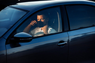 Portrait of man wearing disposable medical facemask in a car during coronavirus outbreak. Safety in the city.