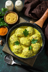 Meatballs with bulgur in sour cream and turmeric sauce in a pan on a dark stone countertop.
